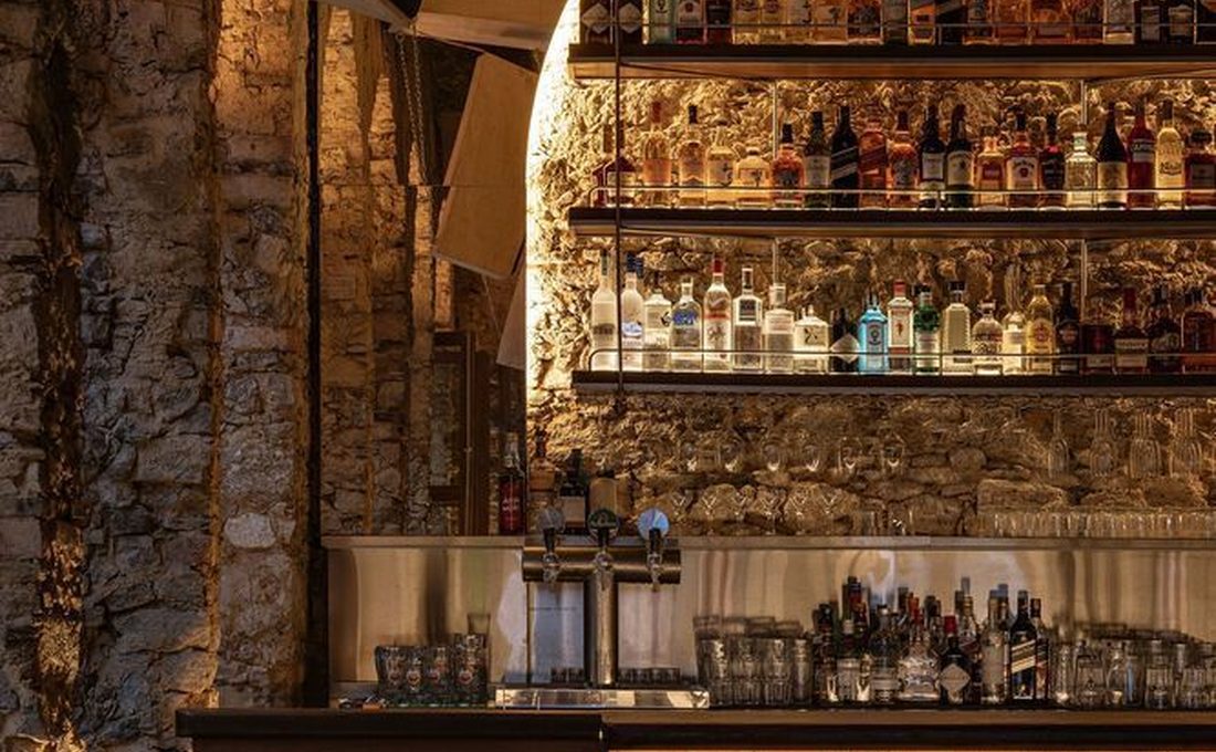 Le bar d'un restaurant en pierre apparente, bouteilles éclairées et tables dressées